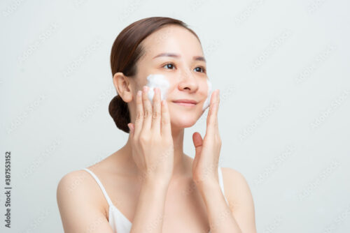 Face skin care. Woman applying facial cleanser on face closeup. Girl using cleansing cosmetic product on skin, washing face on light background